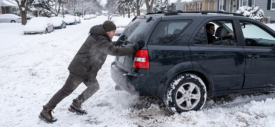 Person pushing a car stuck in snow